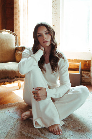 Woman in a white outfit sitting on the floor in a sunlit room.