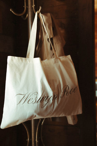 White tote bag with 'Westyn Roe' branding hanging on a hook.