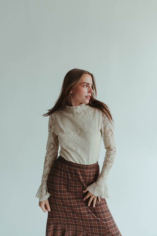 Woman wearing a white lace top and plaid skirt against a plain background