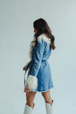 Woman wearing a denim dress with fur accents against a light background