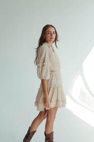 Woman wearing a beige dress with long hair standing against a light background