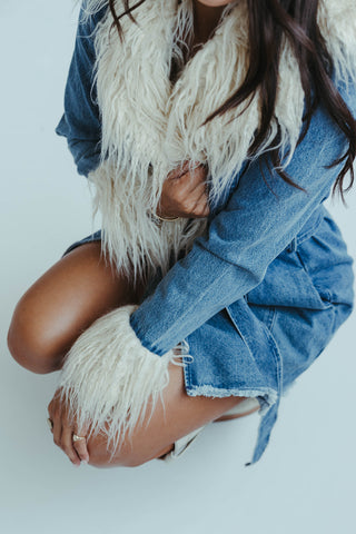 Person wearing a denim jacket and white scarf on a light background
