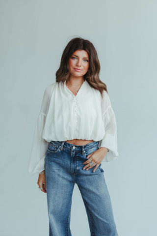 Woman wearing a white blouse and blue jeans against a light gray background