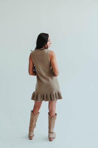Woman wearing a beige dress with ruffled hem and matching boots on a light background