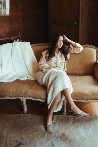 Woman in a beige dress sitting on a vintage couch in a warm, wooden interior.