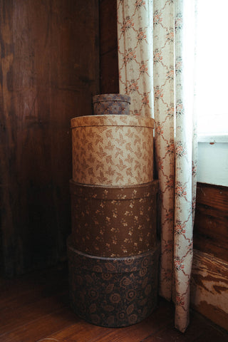 Stack of patterned cylindrical boxes against a floral curtain.