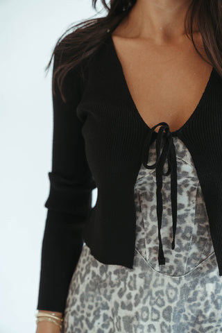 Person wearing a black cardigan over a patterned dress with a white background