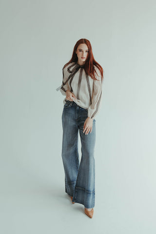 Woman wearing a patterned blouse and blue jeans on a light gray background