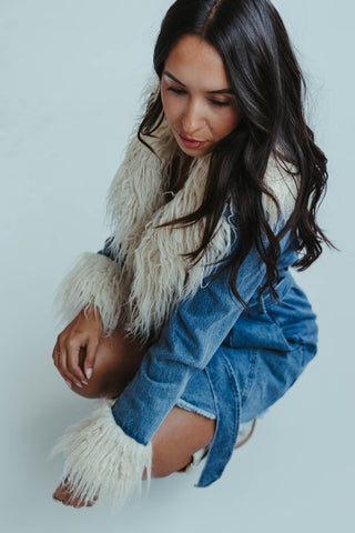 Woman wearing a denim dress with a white shawl against a light background