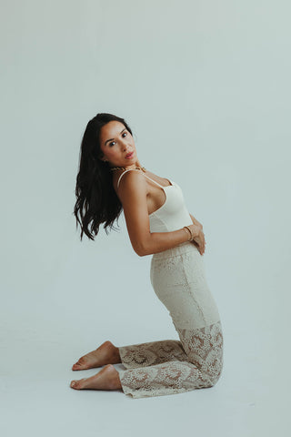 Woman in a white top and patterned pants sitting on a light gray background