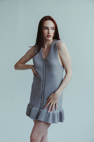 Woman wearing a gray sleeveless dress against a plain background
