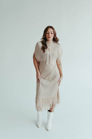 Woman wearing a beige dress with a poncho and white boots on a light background