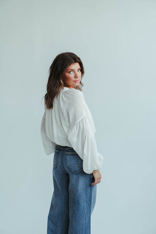 Woman wearing a white blouse and blue jeans against a light gray background