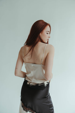 Woman wearing a white satin top and black lace skirt against a light gray background
