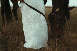 Person in a white lace dress standing next to a horse in a field