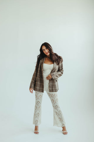 Woman wearing a plaid blazer over a white lace outfit on a light gray background
