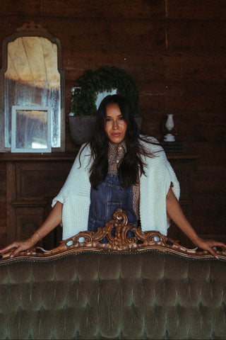 Woman sitting behind a wooden desk with a mirror in a rustic room.