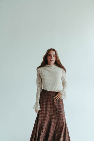 Woman wearing a white lace top and plaid skirt against a plain background