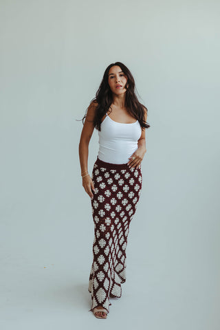 Woman wearing a white tank top and patterned skirt on a plain background