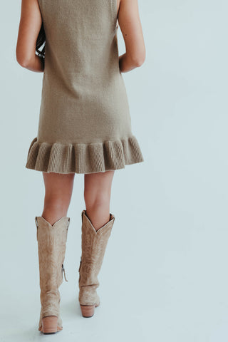 Person wearing a beige dress with ruffled hem and matching boots on a light background