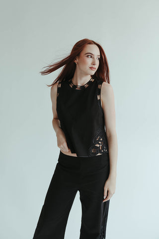 Woman wearing a black sleeveless top with cut-out details against a plain background