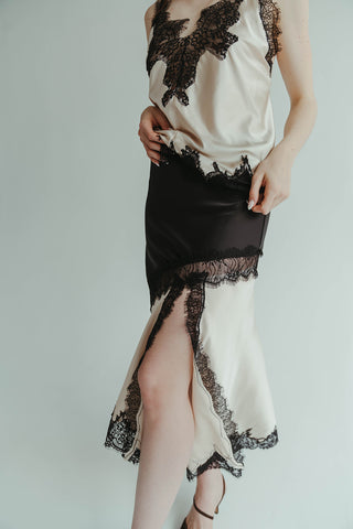 Woman wearing a black and white lace dress with a high slit on a plain background