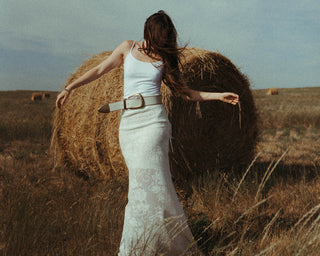 Woman in a white dress standing in a field with hay bales.