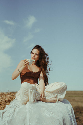 Woman sitting on a rock in a field, holding a mug.