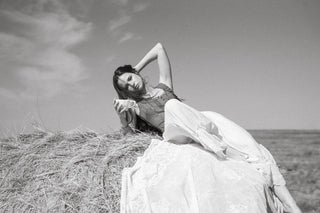 Woman in a dress sitting on a hay bale against a cloudy sky